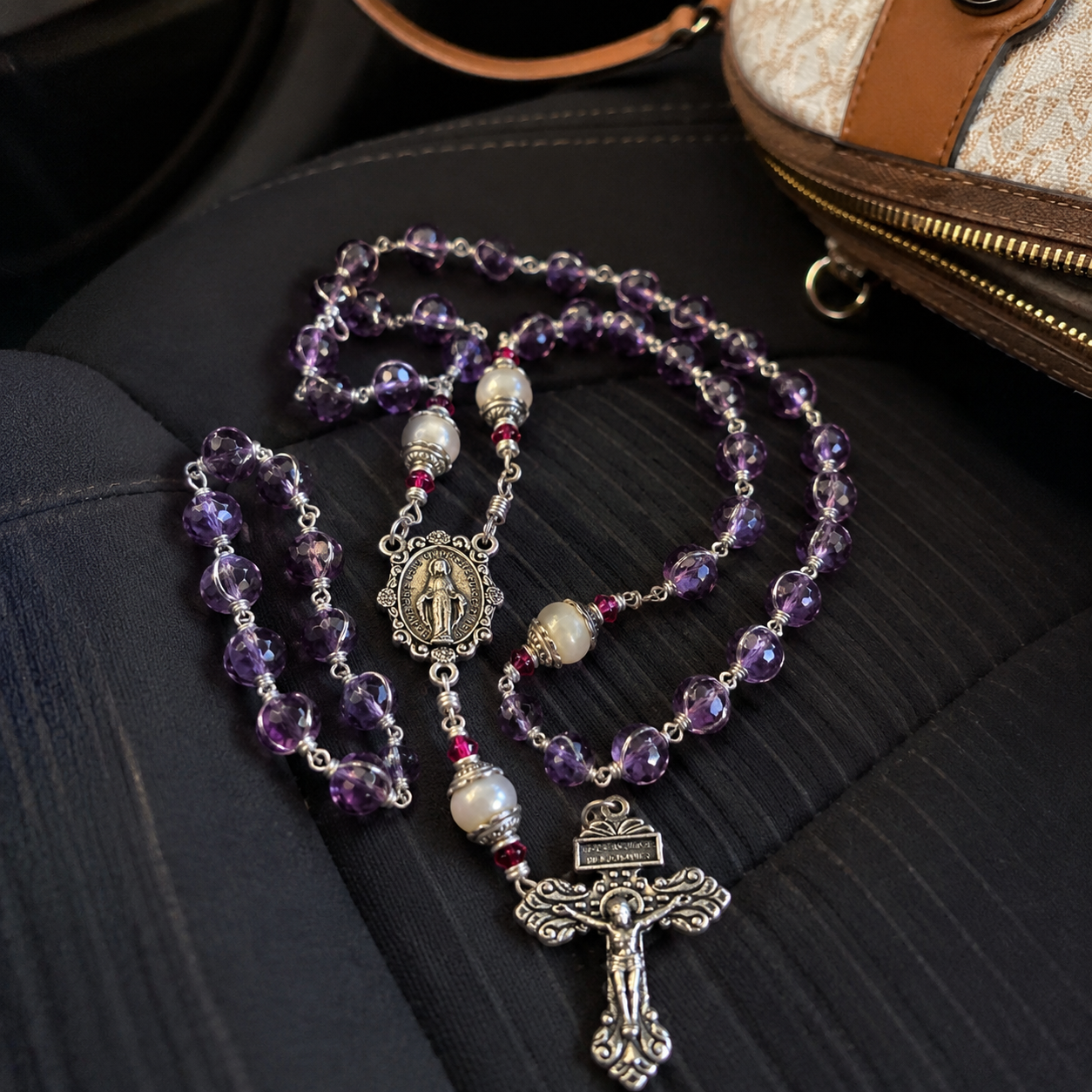 Amethyst pearl rosary resting on a car seat beside a purse